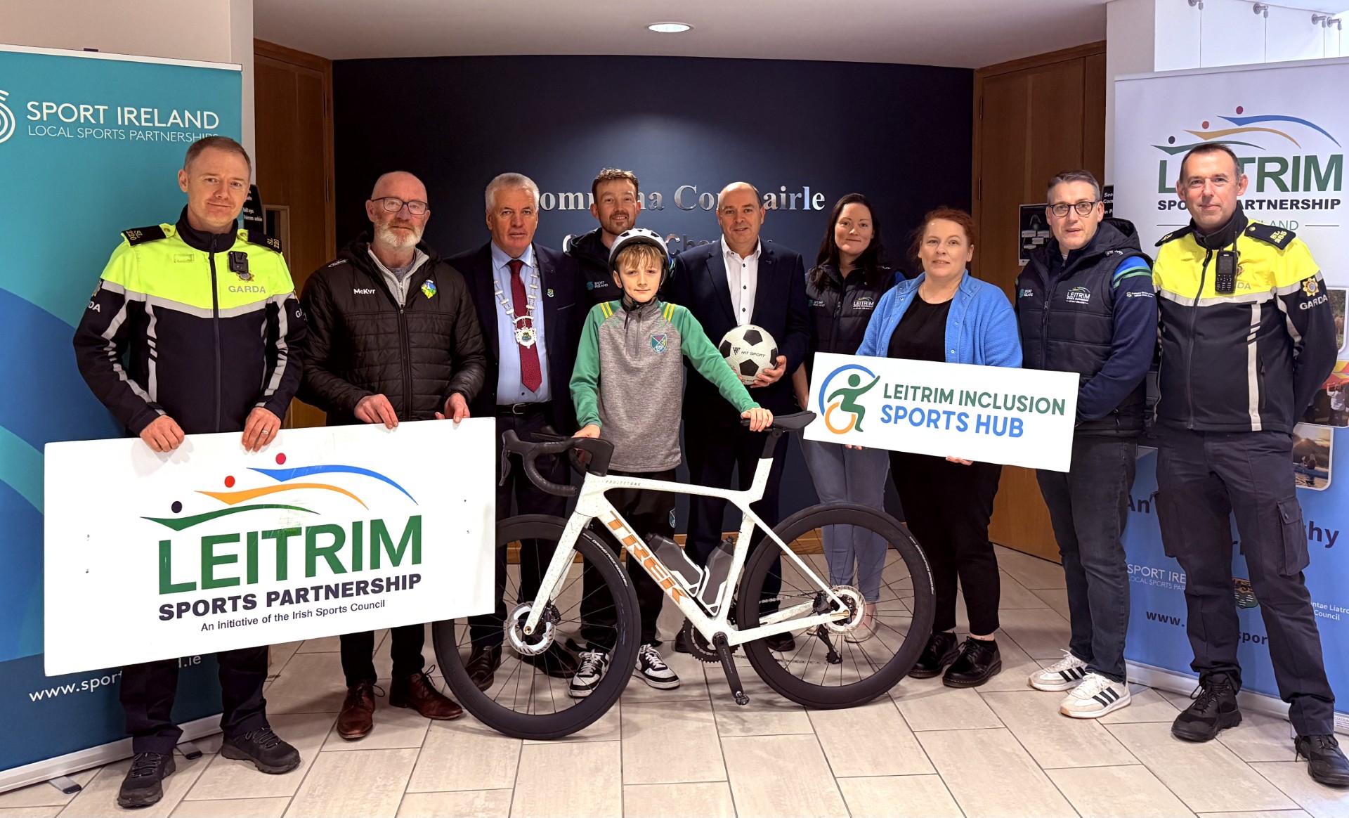 Photo of nine people and a child with a bike football and banners at the launch of Sports Star Awards 2025
